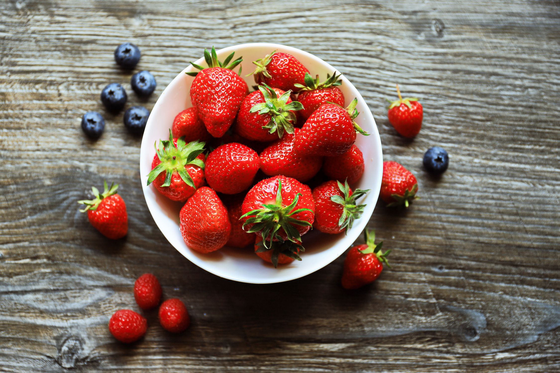 A bowl of fresh mixed berries on a rustic wooden table, shot from above - British Berries Guide