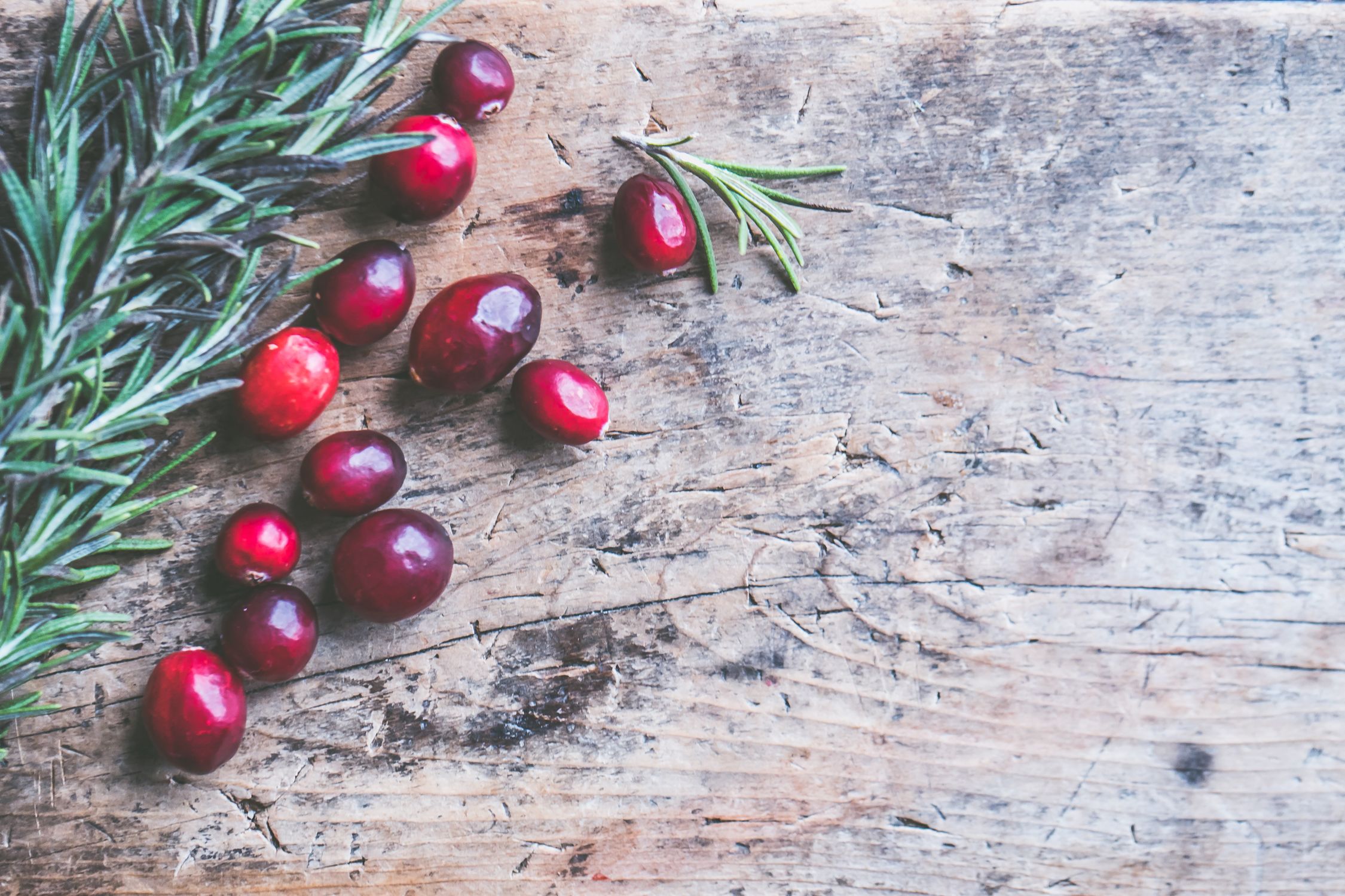 Fresh cranberries and rosemary sprigs scattered on a rustic wooden surface